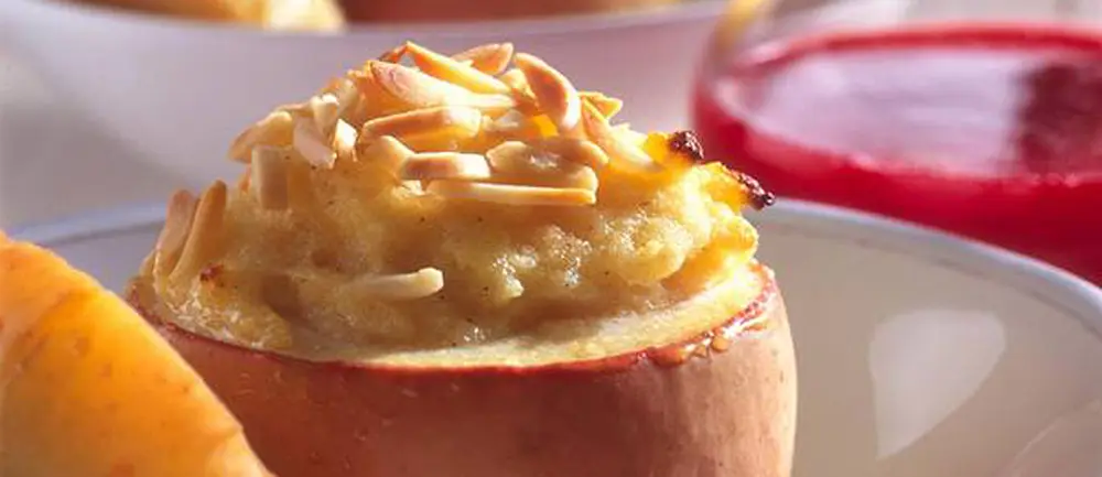 Gefüllter Bratapfel mit goldbrauner Grießfüllung und hellen Nussblättchen, daneben rote Fruchtsoße
