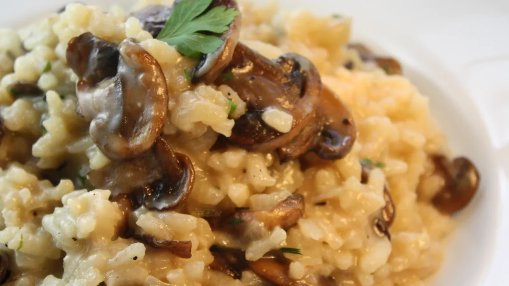 Cremiges Risotto mit gebratenen Pilzen und Petersilie auf einem weißen Teller
